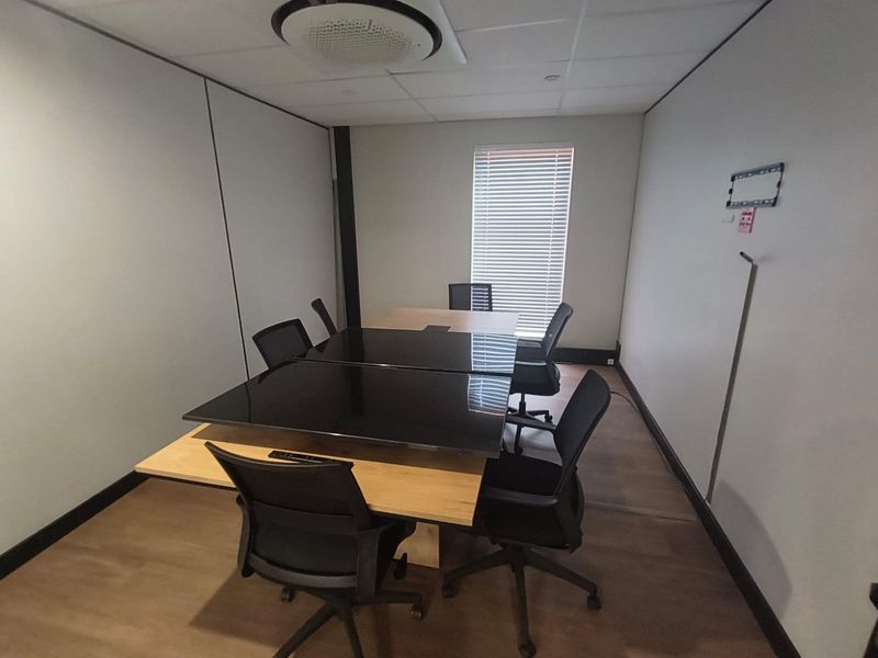 A functional office meeting room featuring laminate flooring, a suspended ceiling with integrated lighting, and window blinds.