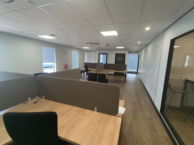 Modern open-plan office space featuring laminate flooring, suspended ceilings with recessed lighting, and integrated workstation partitions.