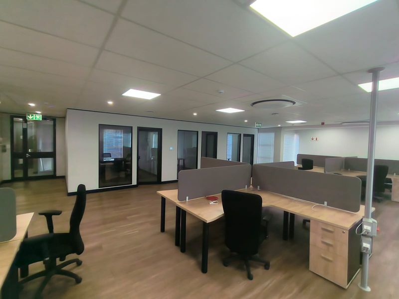 Modern open-plan office space featuring laminate flooring, suspended ceilings with recessed lighting, and glass-partitioned private offices.