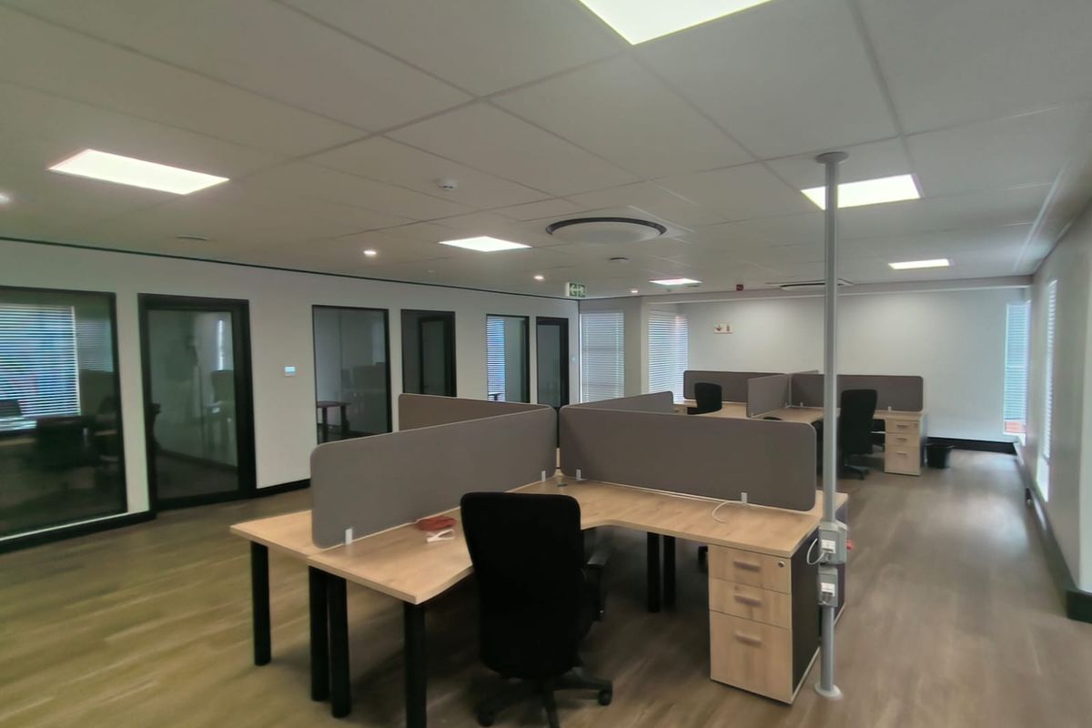 Modern open-plan office space featuring suspended ceilings, recessed lighting, glass-partitioned private offices, and durable laminate flooring.