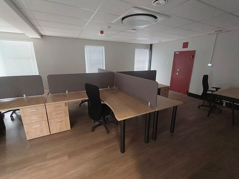 A functional office space featuring a suspended ceiling with integrated air conditioning, laminate flooring, and multiple windows with venetian blinds.
