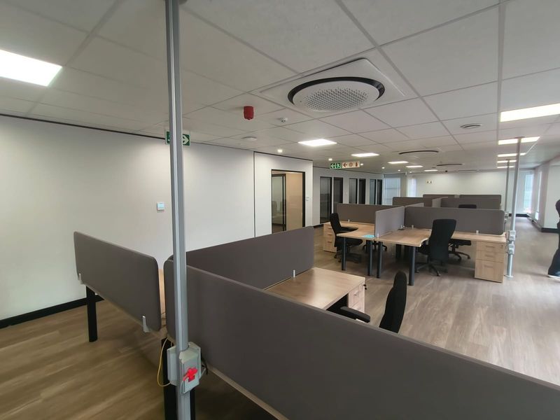 Modern open-plan office space featuring suspended ceilings, recessed lighting, integrated cassette air conditioning, and functional built-in workstation partitions.