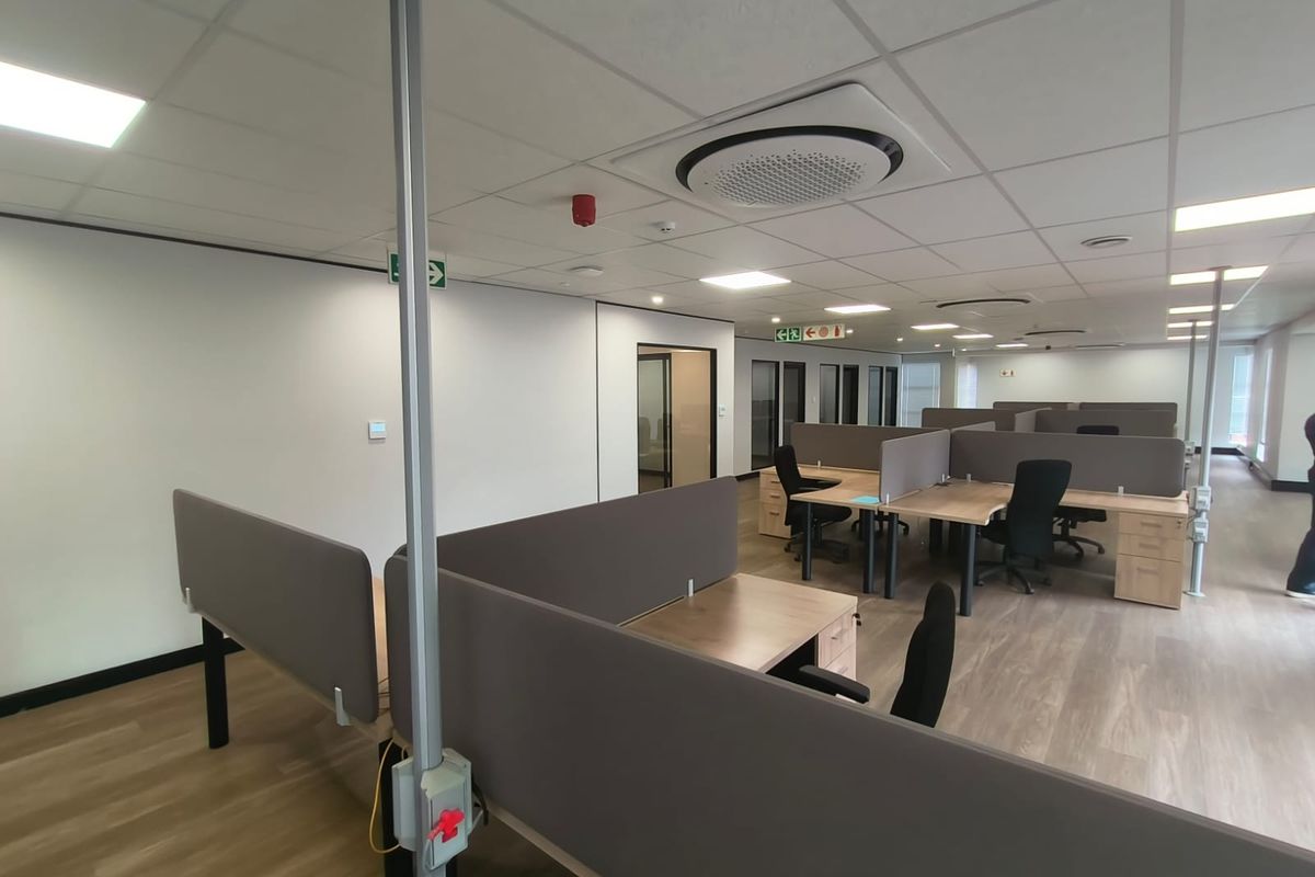 Modern open-plan office space featuring suspended ceilings, recessed lighting, integrated cassette air conditioning, and functional built-in workstation partitions.