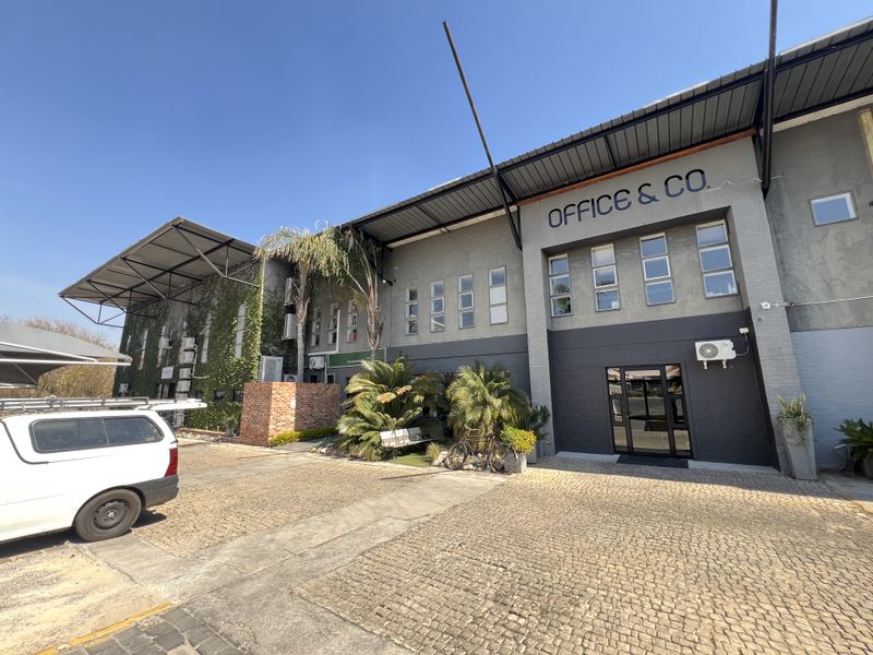 Front exterior view of a commercial office building featuring a cobblestone driveway, brick facade, and modern metal roof structure.