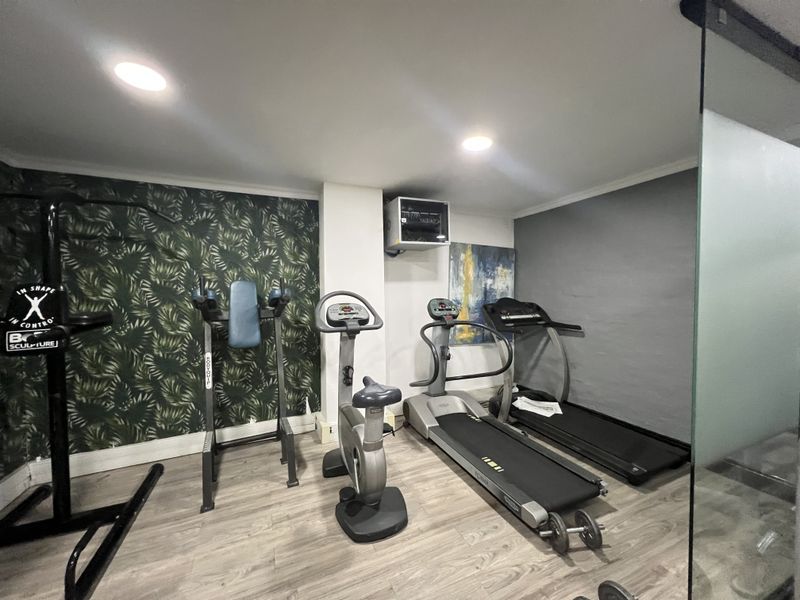 A dedicated gym space featuring laminate flooring, recessed lighting, and a glass partition wall, providing a functional area for fitness equipment.