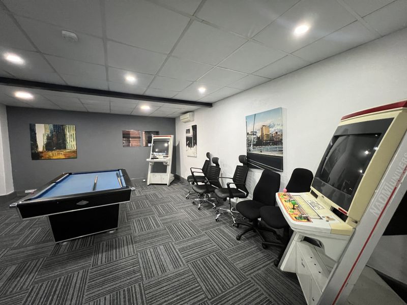 A modern office breakout space featuring carpet tiles, recessed downlighting, and a suspended ceiling, currently utilized as a recreational area.