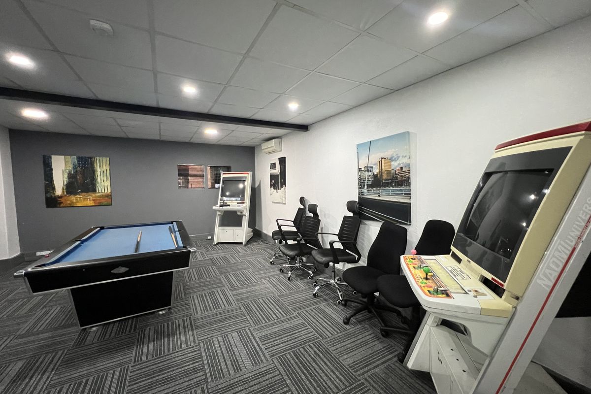 A modern office breakout space featuring carpet tiles, recessed downlighting, and a suspended ceiling, currently utilized as a recreational area.