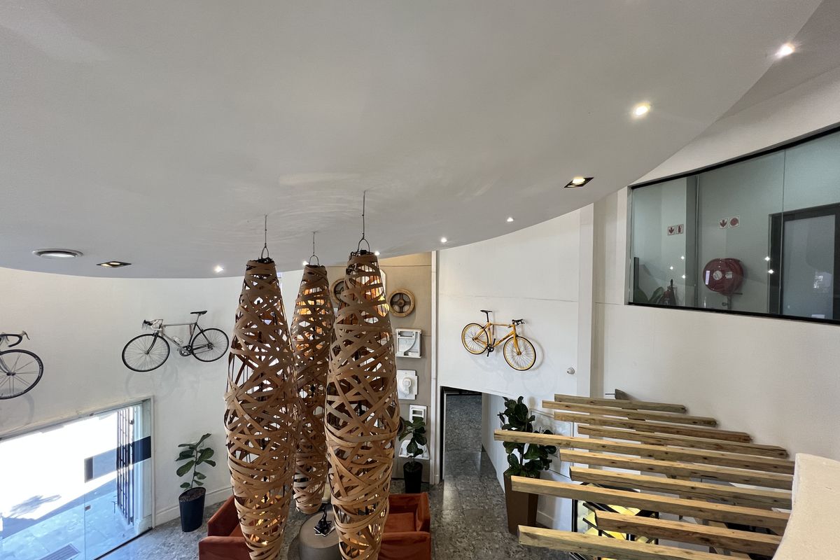 Modern office entrance lobby featuring high ceilings, decorative pendant lighting, stone flooring, and a glass-partitioned office space.