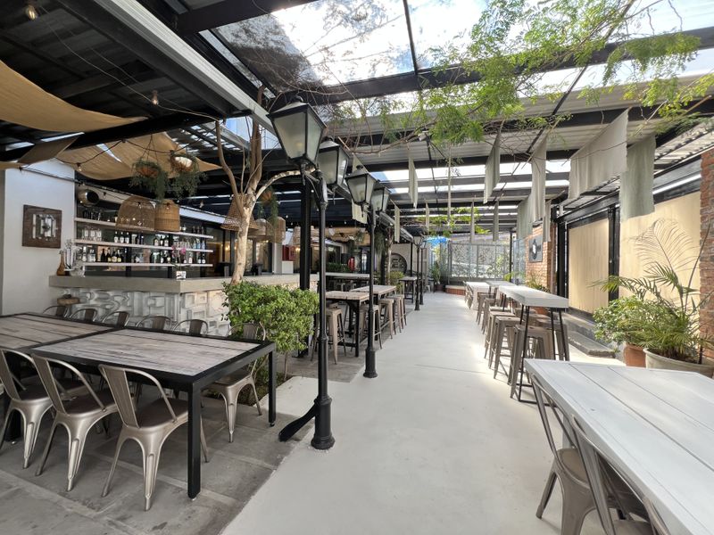 A spacious covered outdoor patio area featuring a built-in bar, glass roofing, and decorative lighting, suitable for office social events or breakout space.