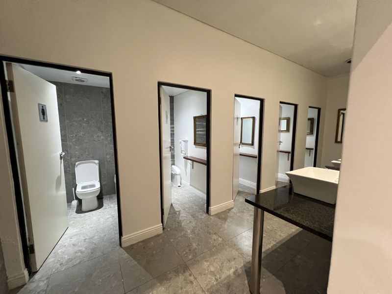 Modern office restroom facility featuring multiple private toilet cubicles, tiled finishes, and a sleek vanity area with a vessel sink.