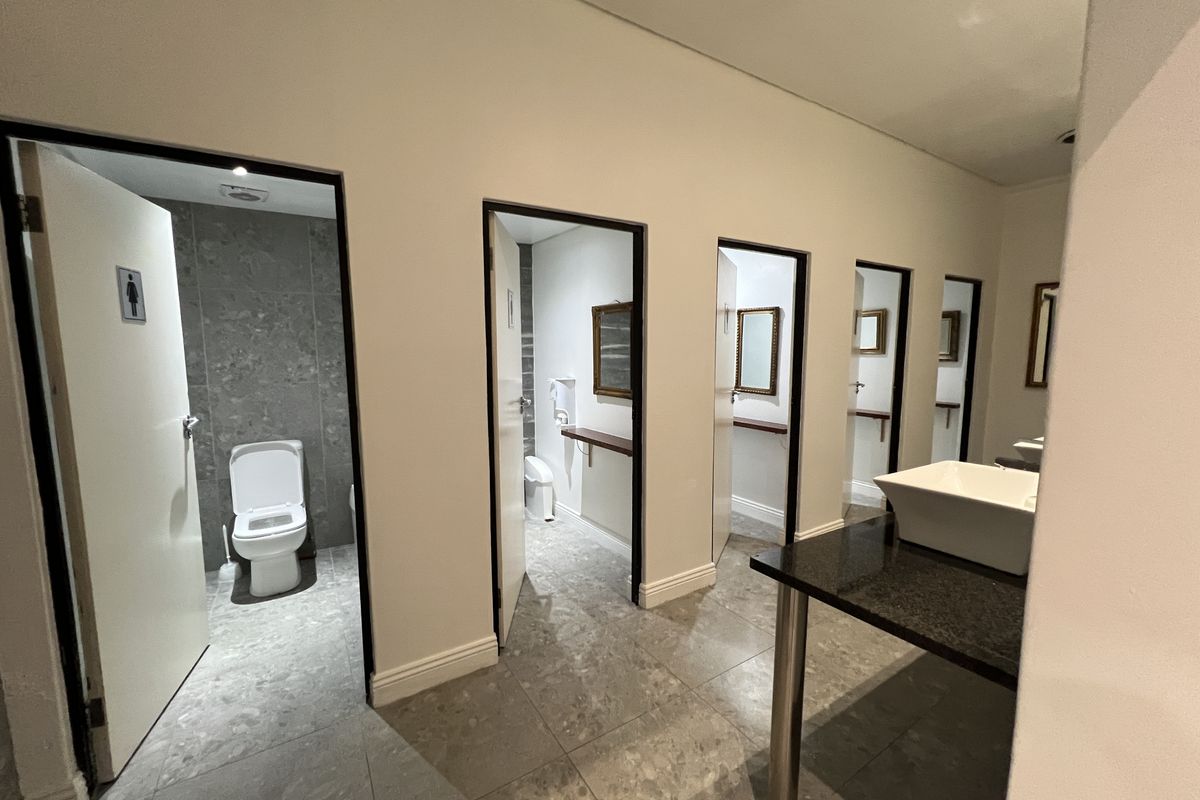 Modern office restroom facility featuring multiple private toilet cubicles, tiled finishes, and a sleek vanity area with a vessel sink.