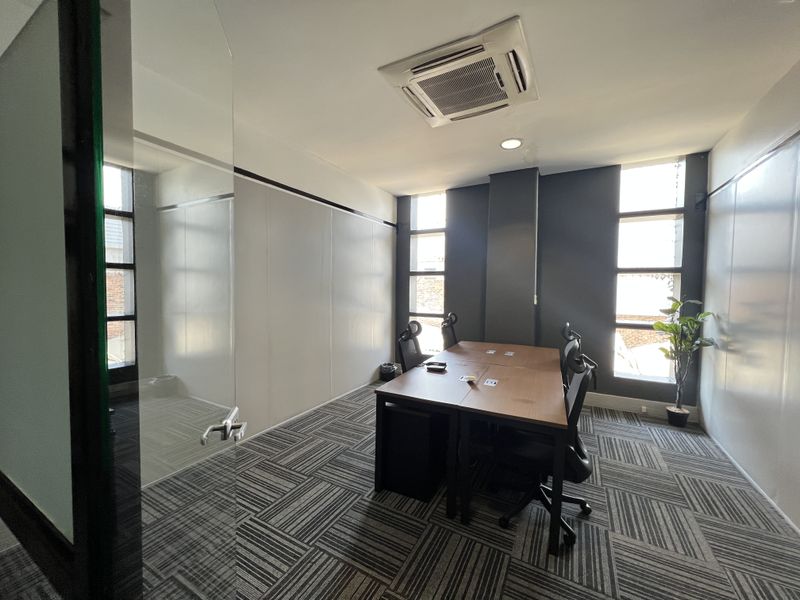 A modern office space featuring carpet tiles, recessed ceiling air conditioning, and large vertical windows providing natural light.