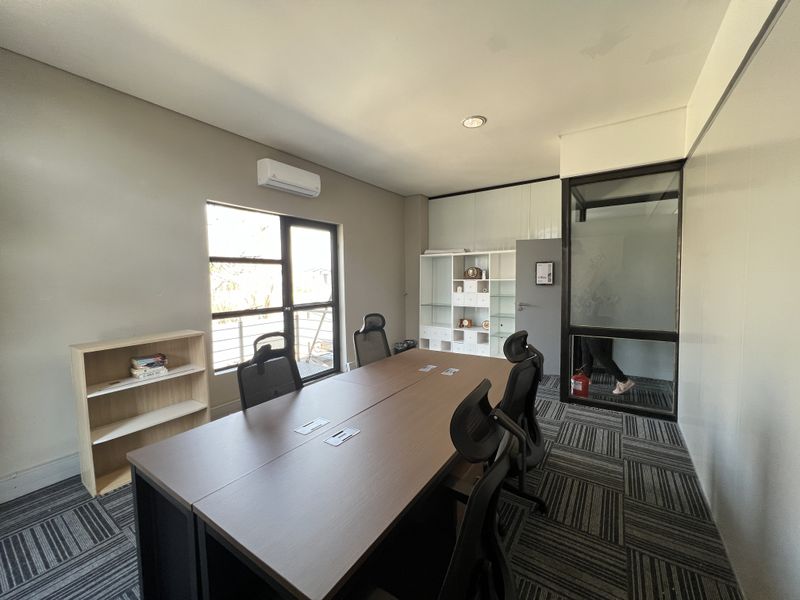 A professional office space featuring carpet tiles, a glass partition wall, built-in shelving, and a wall-mounted air conditioning unit.