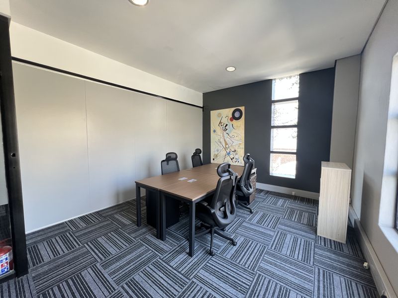 A modern office space featuring patterned carpet tiles, recessed ceiling lighting, and a tall vertical window providing natural light.