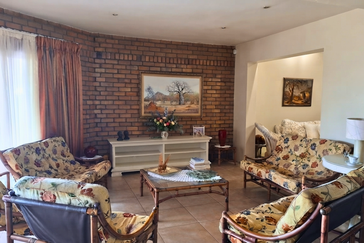 A spacious living room featuring an exposed brick feature wall, tiled flooring, and direct access to an outdoor patio area through sliding glass doors.