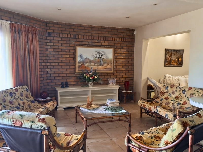 A spacious living room featuring an exposed brick feature wall, tiled flooring, and direct access to an outdoor patio area through sliding glass doors.