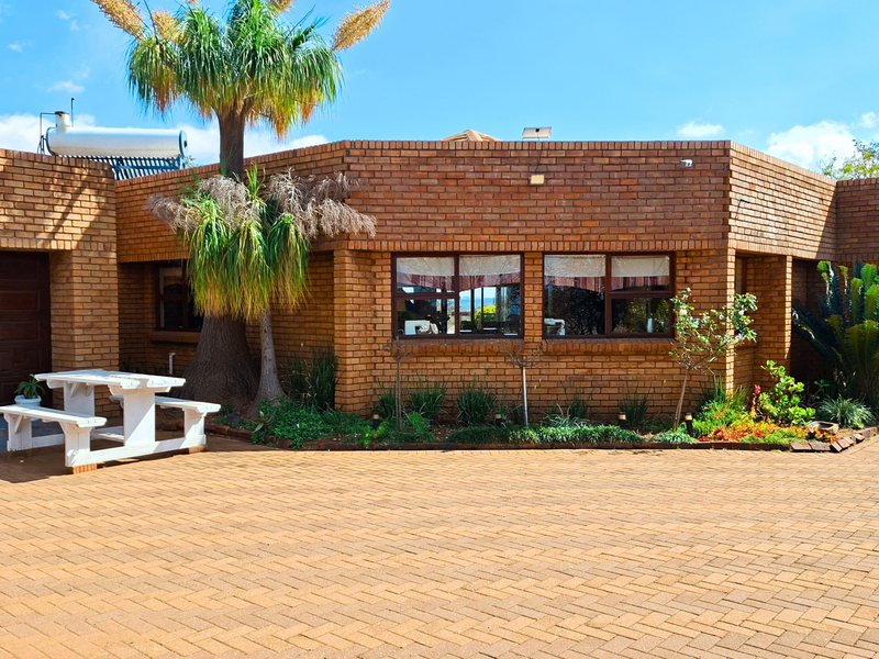 Front elevation of a face-brick small holding property featuring a paved driveway, integrated garage, and solar water heating system.