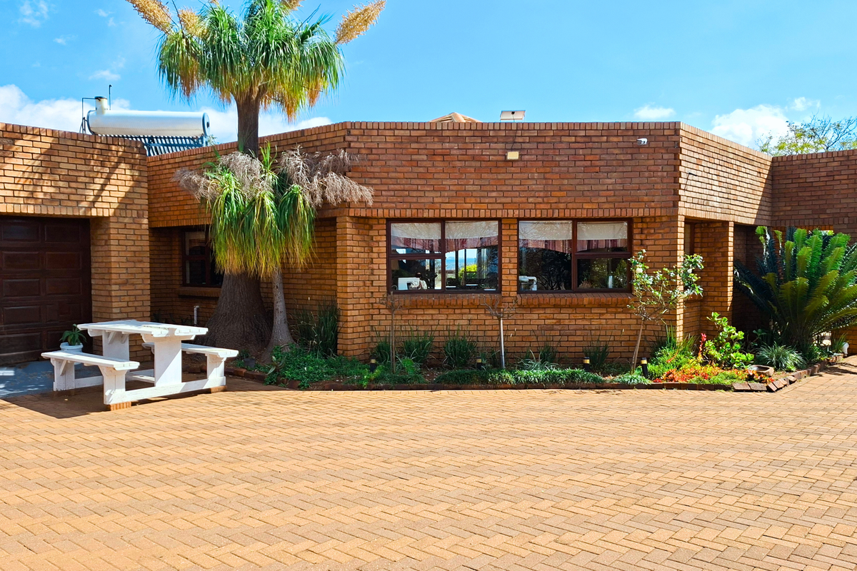 Front elevation of a face-brick small holding property featuring a paved driveway, integrated garage, and solar water heating system.
