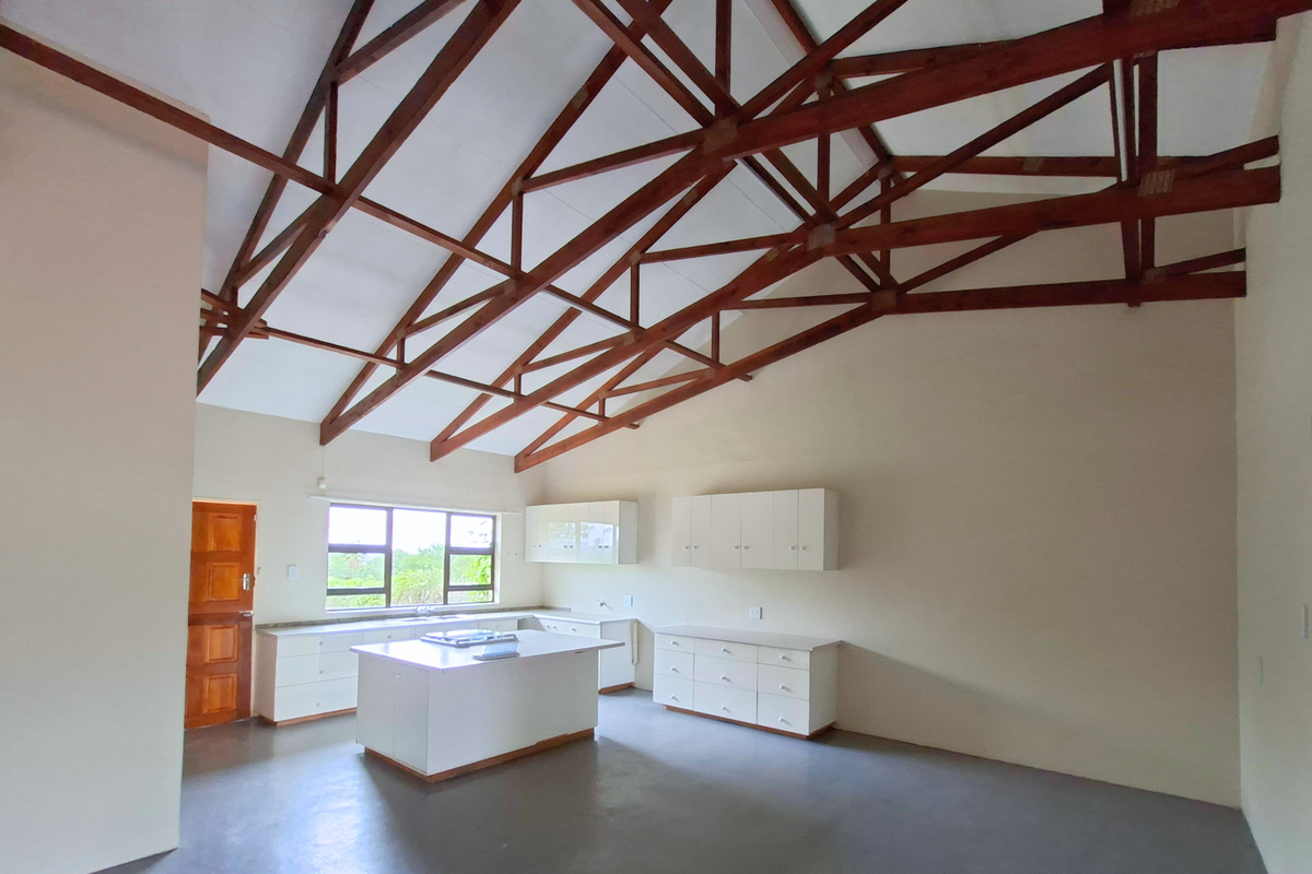 Spacious open-plan kitchen featuring high vaulted ceilings with exposed timber trusses, a central island, and ample built-in cabinetry.