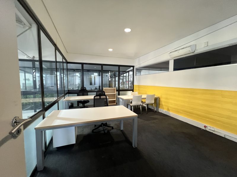 A functional office space featuring glass partition walls, recessed lighting, and a split-system air conditioner, providing a bright and professional work environment.
