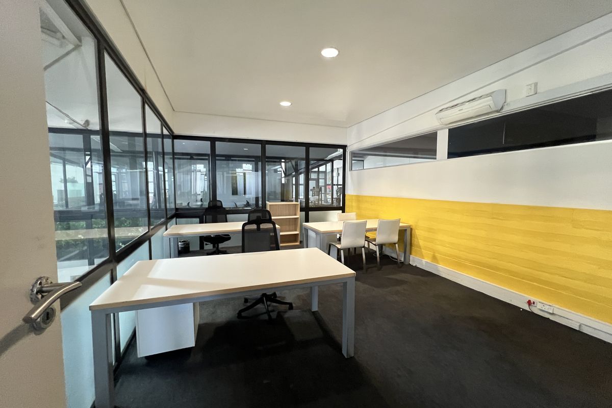 A functional office space featuring glass partition walls, recessed lighting, and a split-system air conditioner, providing a bright and professional work environment.
