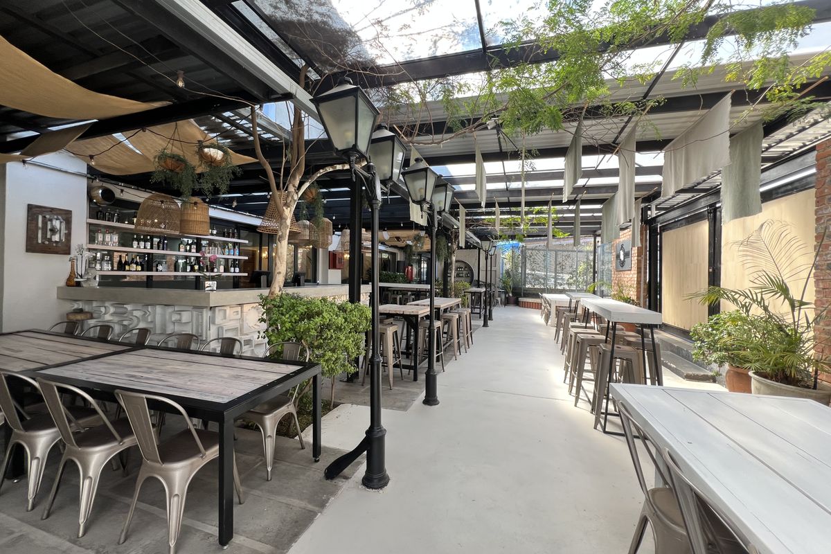 A spacious covered outdoor patio area featuring a built-in bar, glass roofing, and decorative lighting, suitable for office social events or breakout space.