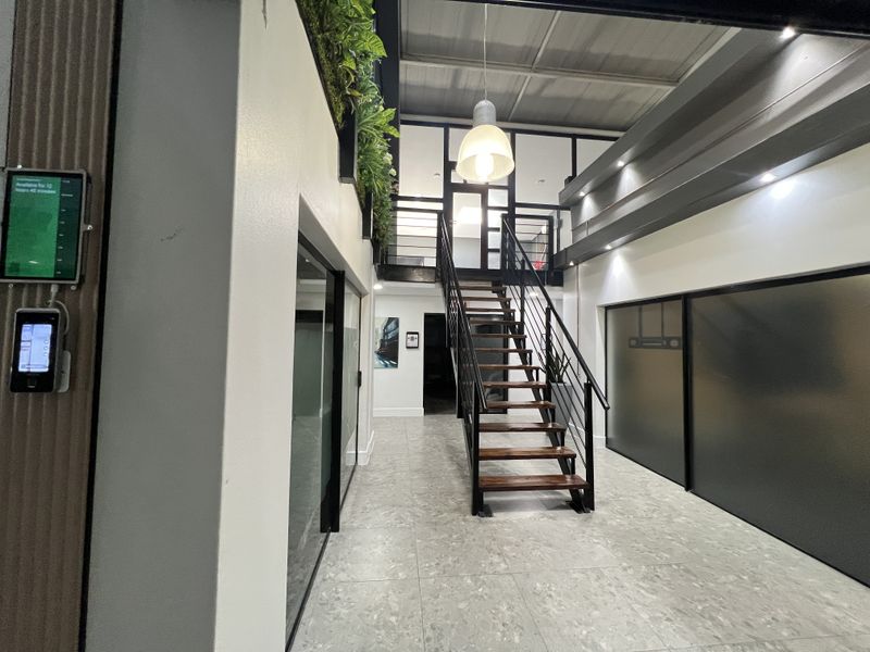 Modern office entrance featuring a sleek staircase leading to a mezzanine level, glass partitions, and contemporary tiled flooring with professional recessed lighting.