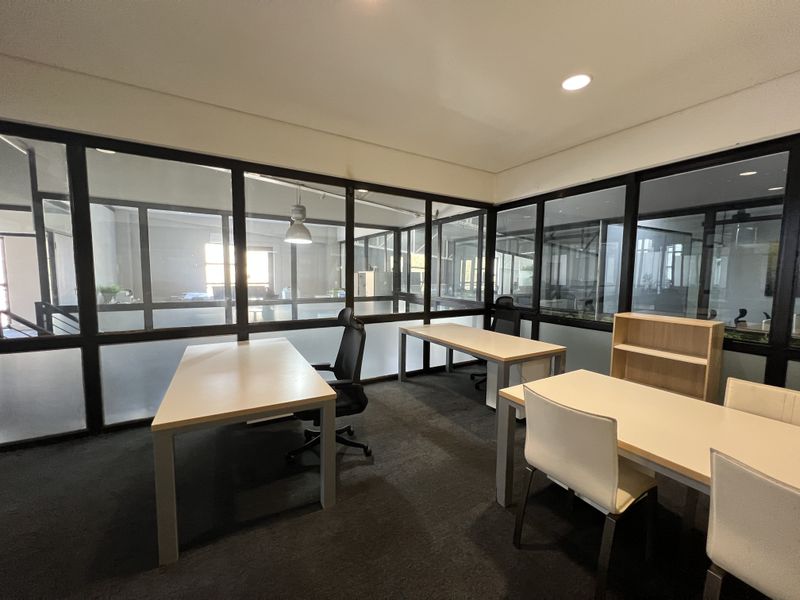 A modern office space featuring black-framed glass partitioning, recessed lighting, and fitted carpeting, providing a professional and bright work environment.