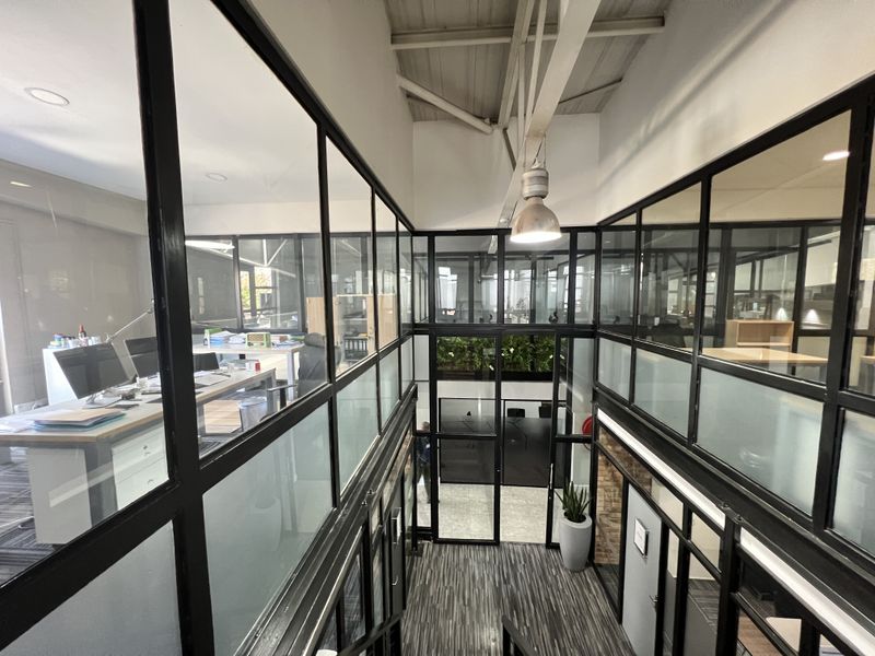 Modern office interior featuring black metal-framed glass partitions, exposed industrial ceilings, and high-quality laminate flooring, creating a bright and professional workspace.