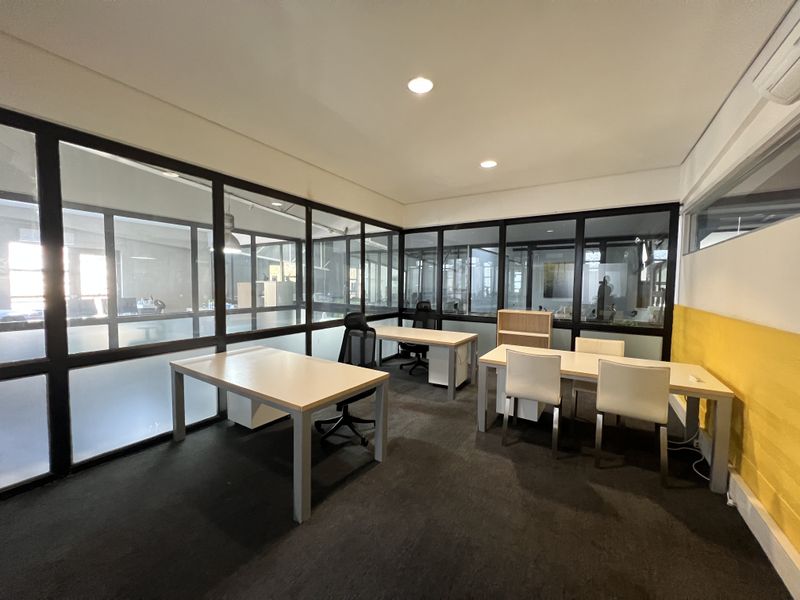 A modern office space featuring black-framed glass partitions, recessed lighting, and carpeted flooring, providing a professional and bright work environment.