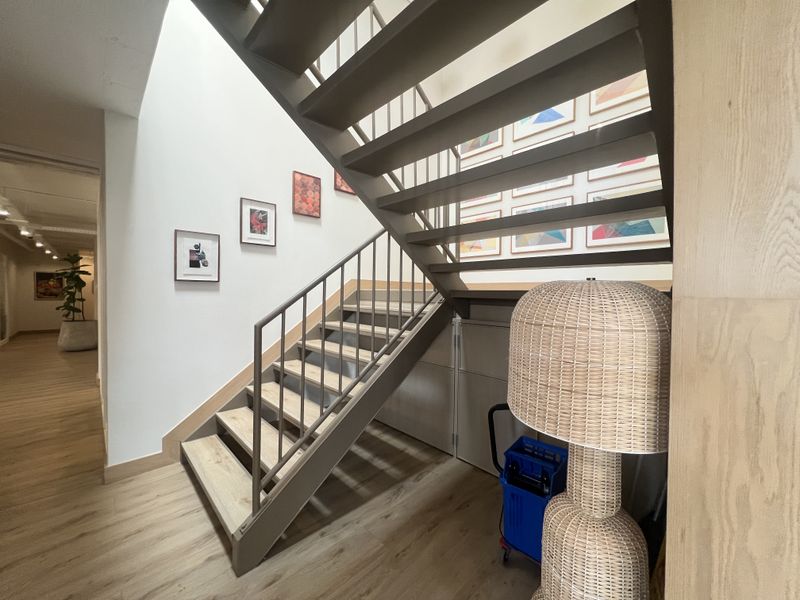 Modern office hallway featuring a contemporary open-tread staircase with metal railings and light wood-look flooring.