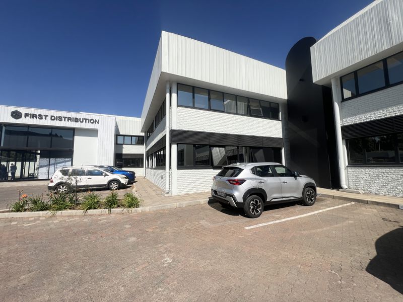 Front exterior view of a modern office building featuring painted brickwork, metal cladding, and dedicated parking bays.