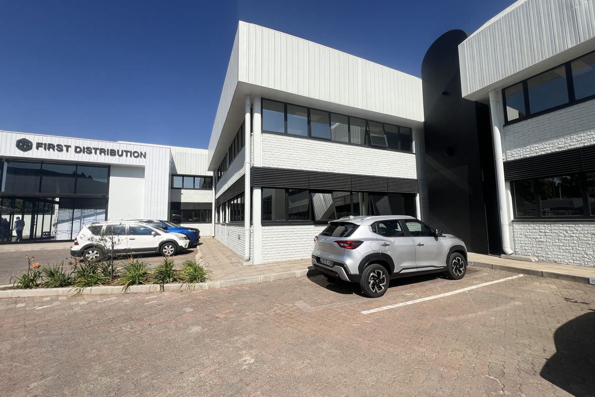 Front exterior view of a modern office building featuring painted brickwork, metal cladding, and dedicated parking bays.
