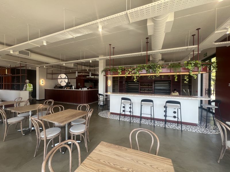 Modern open-plan office cafe area featuring polished concrete floors, exposed industrial ceiling services, and a custom built-in service counter with integrated shelving.