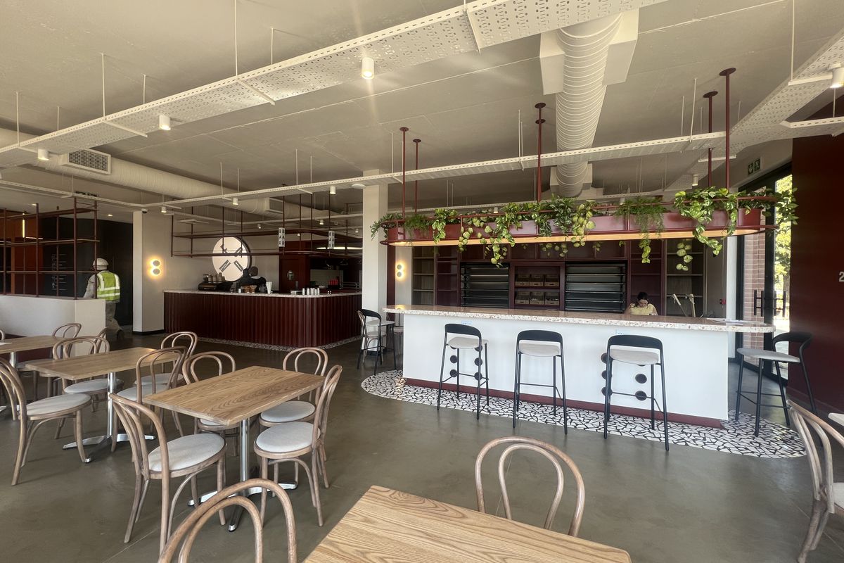 Modern open-plan office cafe area featuring polished concrete floors, exposed industrial ceiling services, and a custom built-in service counter with integrated shelving.