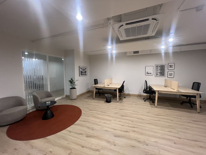 A modern, well-lit office space featuring laminate wood flooring, a glass partition wall, and integrated ceiling-mounted air conditioning.