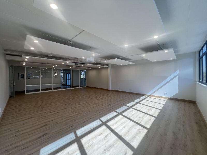 A bright, modern open-plan office space featuring laminate wood flooring, suspended acoustic ceiling panels, and glass partitioning for a professional, airy work environment.