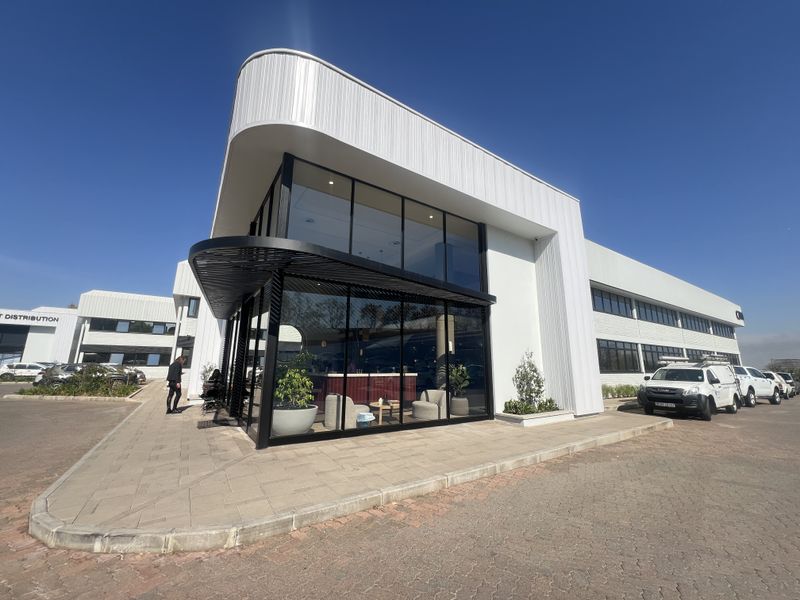 Modern commercial office building featuring extensive glass curtain walling, sleek metal cladding, and a paved entrance area with a contemporary black metal awning.