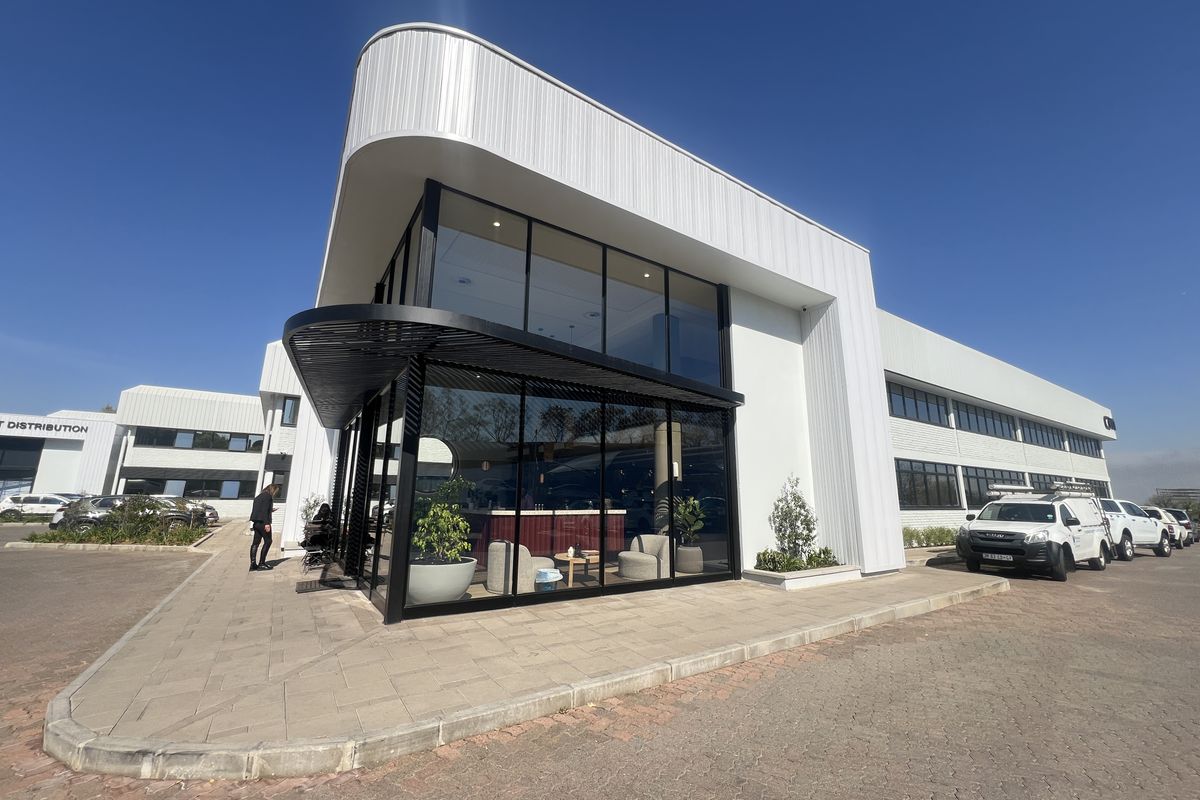 Modern commercial office building featuring extensive glass curtain walling, sleek metal cladding, and a paved entrance area with a contemporary black metal awning.
