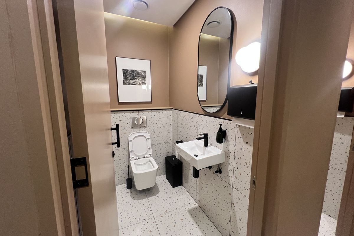 Modern office restroom featuring high-end terrazzo tiling, a wall-mounted basin with black fixtures, and a sleek wall-hung toilet with a concealed cistern.