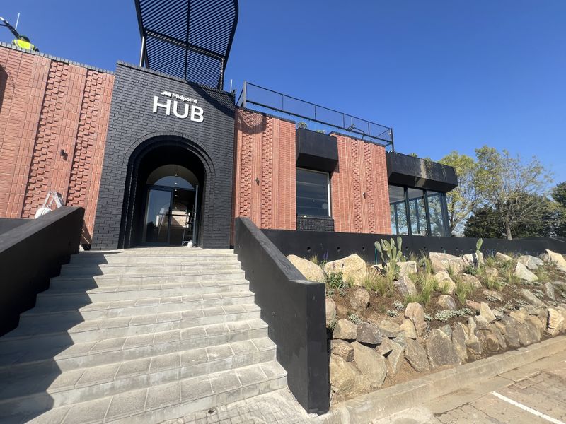 Modern office building entrance featuring a striking brick facade, stone landscaping, and a prominent arched doorway with a metal pergola structure.