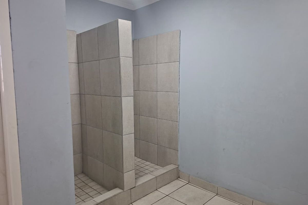 A functional bathroom area featuring dual tiled shower stalls with built-in partitions and neutral floor tiling.