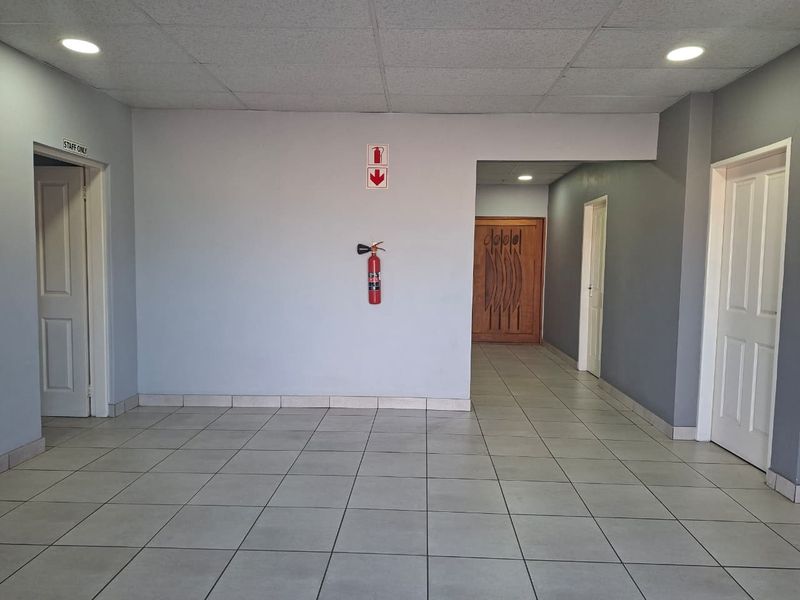 A clean, well-lit industrial hallway featuring neutral grey walls, tiled flooring, and multiple access doors.