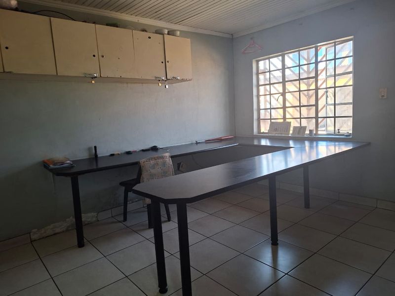 Functional office space featuring built-in desk workstations, overhead storage cabinetry, tiled flooring, and a window with security bars.