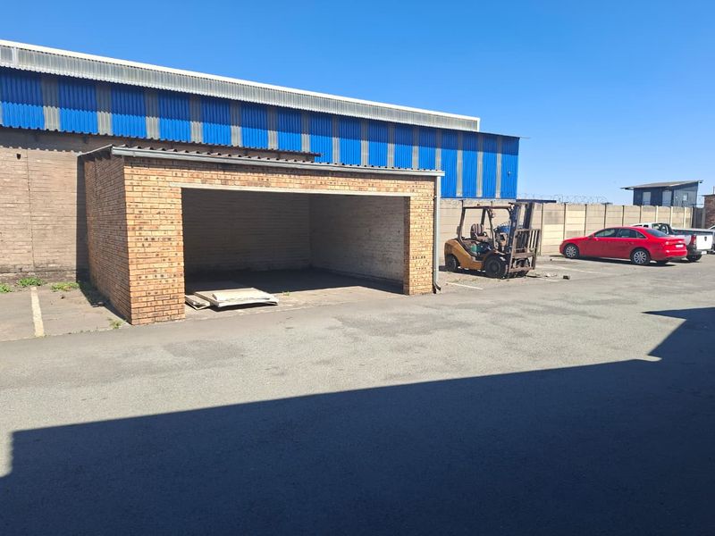 Exterior view of an industrial property featuring a brick-built open storage bay, corrugated metal cladding, and paved yard area.