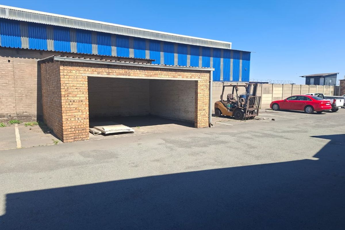 Exterior view of an industrial property featuring a brick-built open storage bay, corrugated metal cladding, and paved yard area.