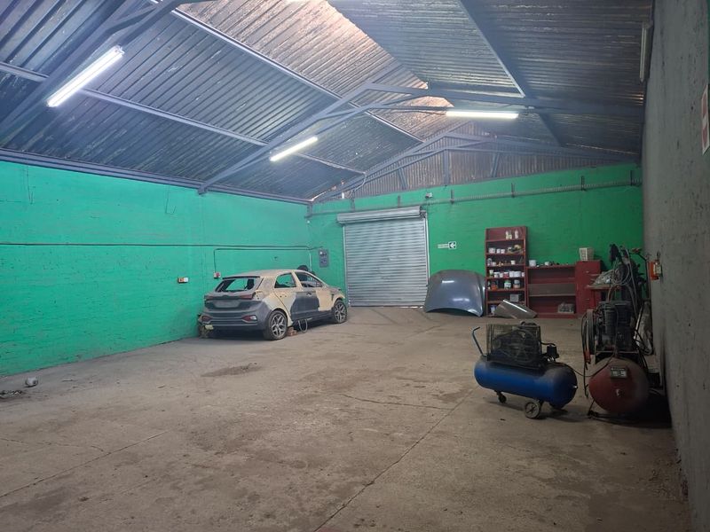 Spacious industrial garage featuring high exposed steel roof trusses, concrete flooring, and a large roller shutter door, suitable for workshop or storage use.