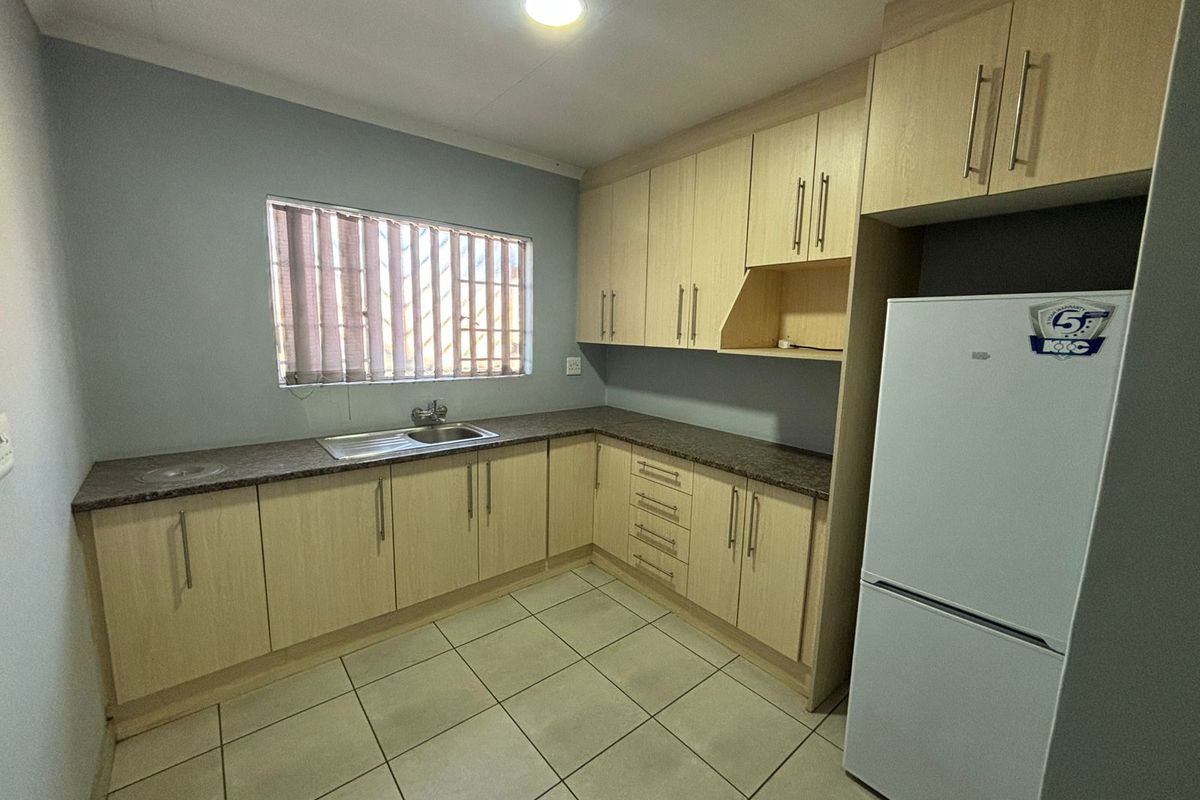 A functional kitchen featuring light wood-finish cabinetry, laminate countertops, a stainless steel sink, and neutral ceramic floor tiles.
