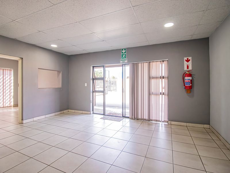 A clean, open-plan industrial entry area featuring neutral grey walls, tiled flooring, recessed lighting, and a functional sliding glass door with emergency exit access.
