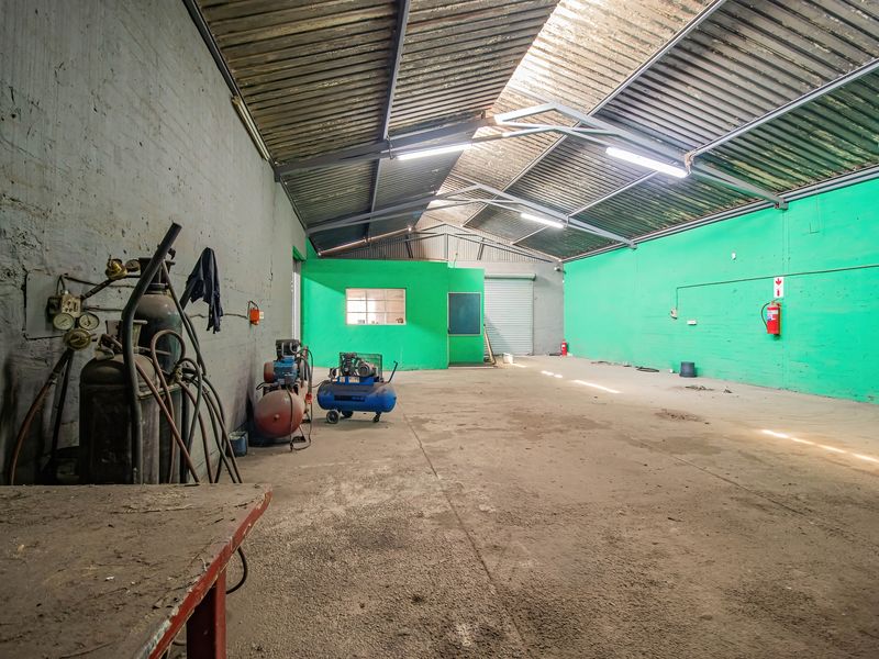 Spacious industrial utility area featuring high ceilings with exposed steel trusses, concrete flooring, and a large roller shutter door for easy access.